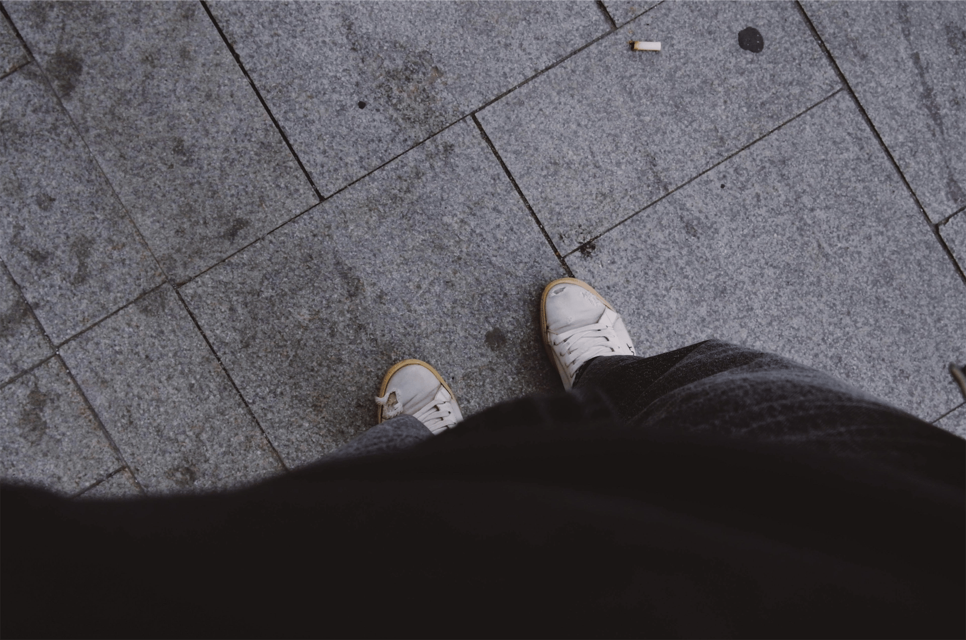 eine Zigarettenkippe auf dem Boden vor den Schuhen eines Rauchers